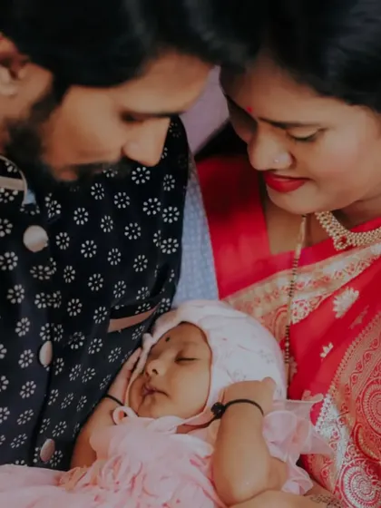 A close-up, intimate portrait of new parents admiring their sleeping baby during a family event.