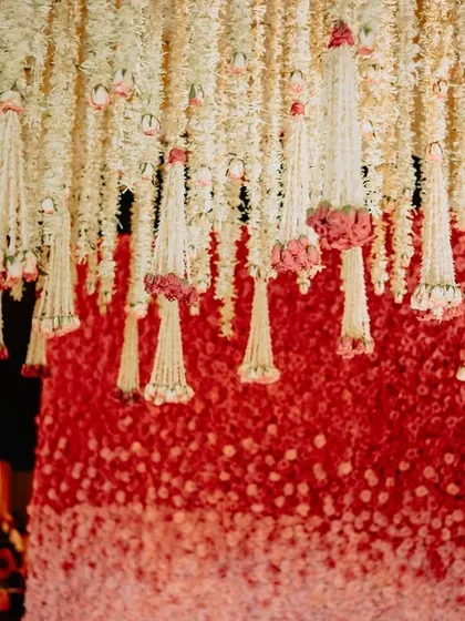 A close-up of the floral backdrop, showing the gradient of red and pink roses, with strings of white jasmine flowers hanging in front for a delicate, layered effect.