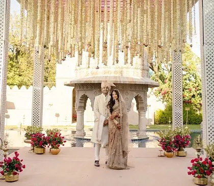 The couple stands at their mandap, framed by hanging floral strings and the architectural beauty of the venue. This setup shows how minimalism can be incredibly impactful and elegant.