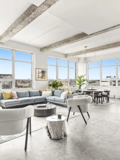 The living room of a New York apartment we designed, featuring an open, light-filled layout with industrial-style exposed beams. The design is tailored for functionality with modern aesthetics, including our iconic Laila Sideboard and Boho Chairs.