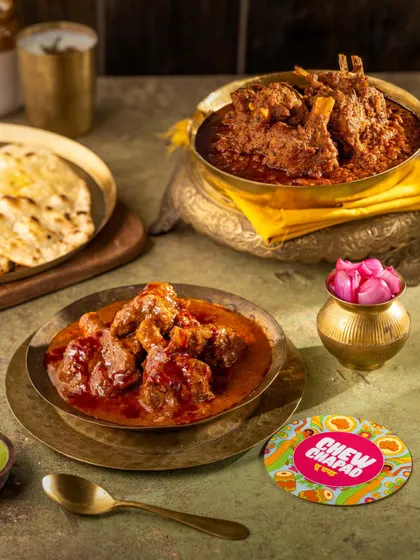 This photo captures a feast of rich, aromatic Mutton Rogan Josh and Mutton Josh. The dishes are presented in traditional serveware with classic accompaniments, creating a scene of indulgent, homestyle Indian dining.