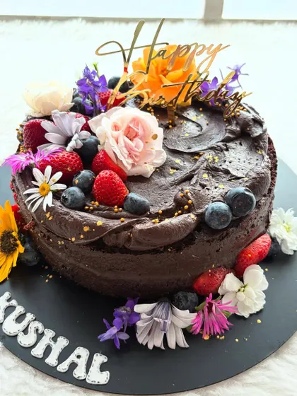A rich chocolate cake adorned with fresh berries and a rainbow of edible flowers. The dark chocolate base makes the colors of the toppings pop.