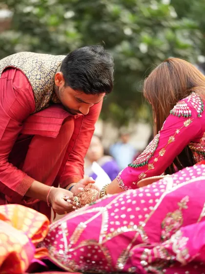 A candid moment where the husband is part of the rituals, with the bride's mehendi-adorned hands in focus.
