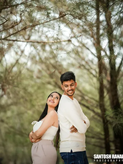 A playful back-to-back pose by a couple in a wooded area, capturing their fun-loving connection.