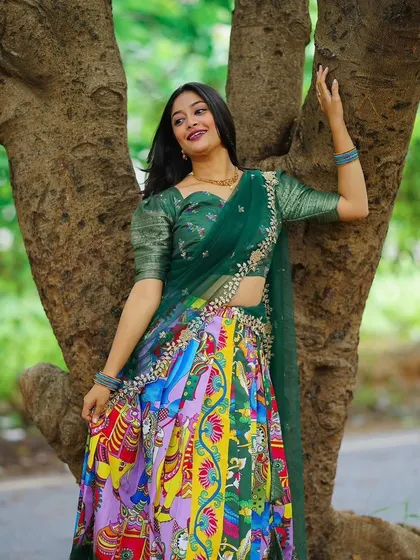 Posed against a tree, this shot highlights the vibrant colors and detailed patterns of the Kalamkari half saree skirt.