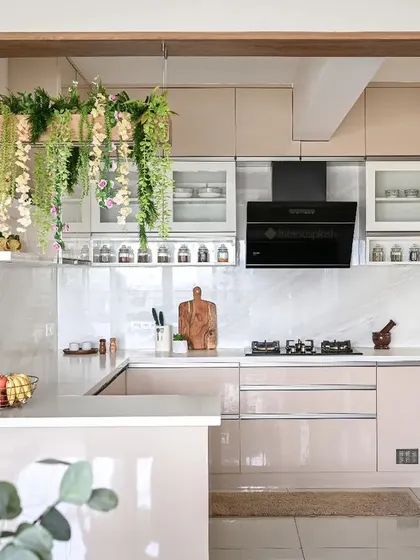 A full view of the pastel-toned kitchen, showing the breakfast counter and the seamless integration of the refrigerator and other appliances. The hanging plants add a vibrant touch of green.