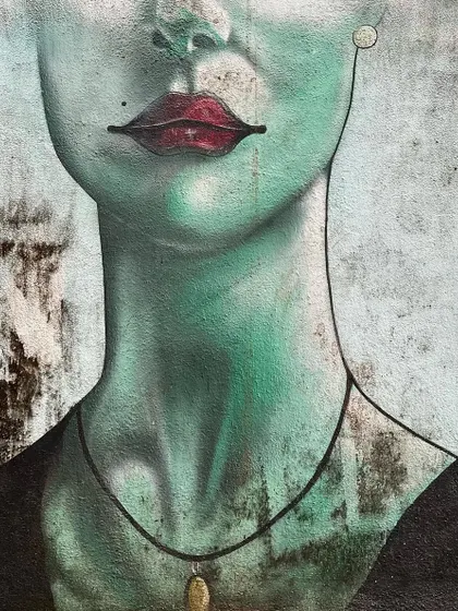A close-up of a serene, green-toned mural of a woman's face on a wall in Bandra.