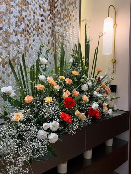 A lush and vibrant floral arrangement designed to beautify a console table for a housewarming party. The mix of red, orange, and white flowers adds a burst of color and joy to the home.