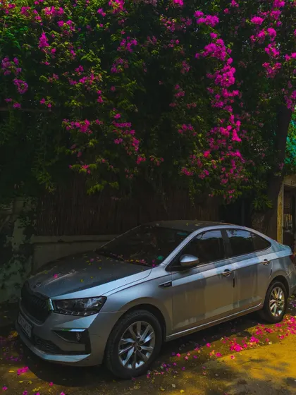 Automotive photography isn't just about mountains. Here, a Skoda Slavia is framed by bougainvillea, creating an aesthetic, urban shot that highlights the car's design and elegance in a beautiful, natural setting.