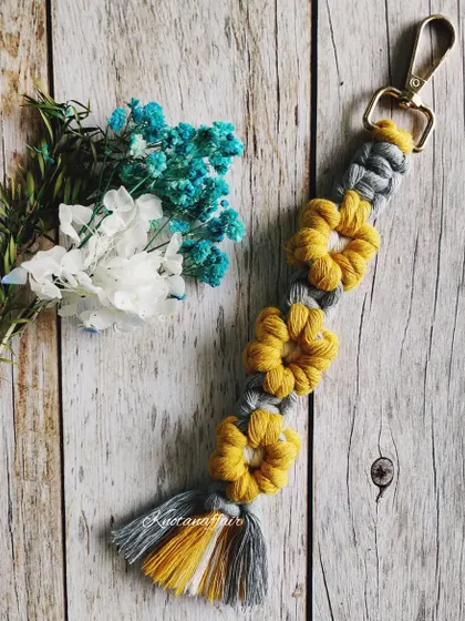 A macrame flower keychain in yellow and grey. This unique design can be used as a bag charm and is a great eco-friendly way of accessorizing.