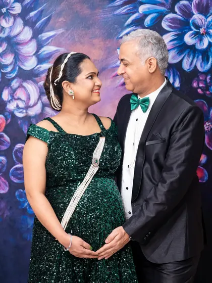 A glamorous indoor maternity portrait. The couple is dressed in formal wear against a beautiful floral backdrop, showing the versatility of shoots I offer, from casual outdoors to elegant indoors.