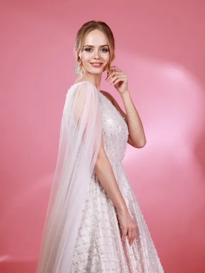 A side-profile portrait of Irina Rudakova in her white gown, with a sheer cape creating a sense of movement and grace.