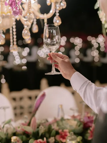 A toast to the happy couple. This image captures the elegant atmosphere of a finale dinner, with beautiful bokeh from the chandeliers and a perfectly set table, a result of months of meticulous planning.