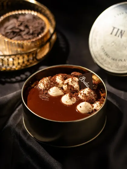 A tiramisu cheesecake in a tin from Bastian. The dark, silky background and golden accents create a feeling of pure luxury and indulgence.