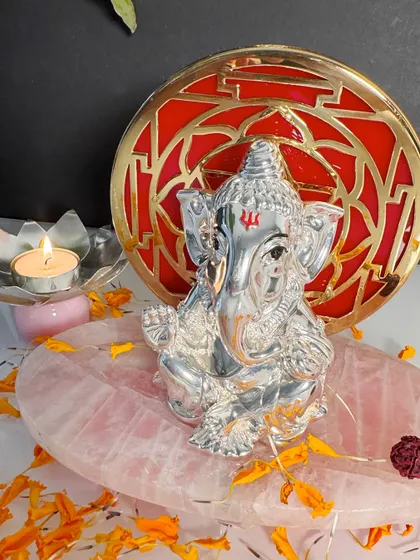 A truly mesmerizing piece, this silver Ganesha idol is set against a striking red and gold geometric backdrop. The polished rose quartz base enhances its beauty, creating a perfect harmony of color, material, and spiritual significance.