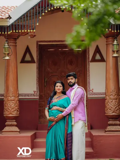 A classic portrait of a couple in front of a traditional house, showcasing their coordinated ethnic outfits.