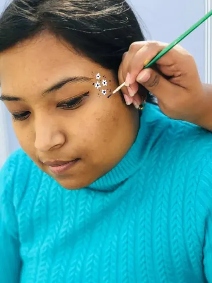 Carefully placing small white flowers on a client's cheek. Precision is important for these delicate designs.