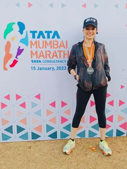 Posing by the Tata Mumbai Marathon banner, Dr. Indu Tandon showcases her finisher's medal. Her journey as a doctor, mother, and national-level athlete is an inspiration to our community.
