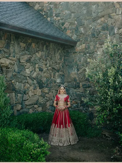 A stunning bridal portrait against a rustic stone wall, the bride's red lehenga providing a vibrant pop of color.