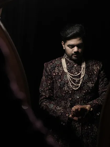 A classic portrait of the groom in a beautifully embroidered sherwani and pearl necklace, checking his watch as he prepares for the ceremony.