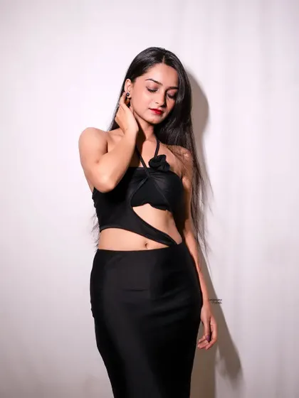 A soft and elegant pose, with the model looking down, highlighting the unique design of her black halter-neck dress.
