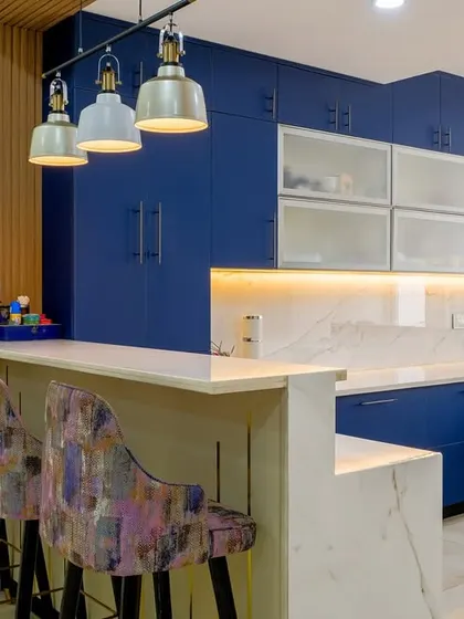 A stunning and functional kitchen design where bold blue cabinets are paired with patterned bar stools and industrial-style pendant lights over the breakfast counter.
