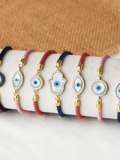 Tie the bond of love and protection with my evil eye rakhis. This image shows a variety of thread bracelets with different evil eye and hamsa designs.