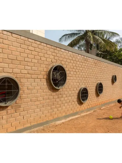 A child plays along the wall of Buddhi School, which features playful circular windows. The building itself becomes a part of the playscape, engaging students at their own scale.