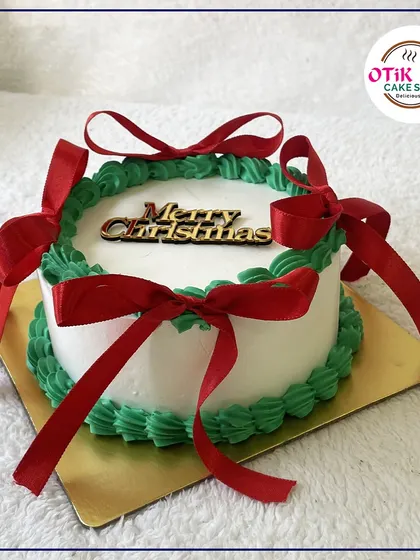 A simple and elegant "Merry Christmas" cake, decorated with a green wreath border and festive red ribbons.