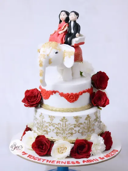 This Indian wedding cake is a celebration of culture and love. It features a hand-sculpted elephant topper with a bride and groom, intricate gold stenciling, and a border of fresh red and white roses.