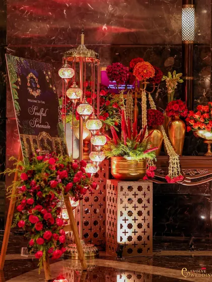 The welcome signage for the 'Soulful Serenade', surrounded by an abundance of red flowers, cascading jasmine, and an elegant Turkish lamp. This sets the tone for the event from the moment guests arrive.