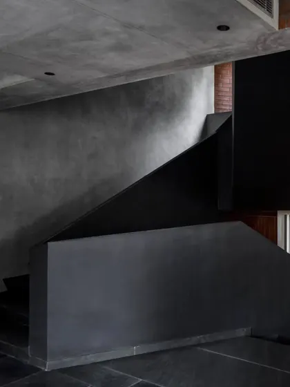 A view of the main staircase in the Brick House, showcasing its monolithic form and the contrast between the smooth black plaster and the surrounding concrete.