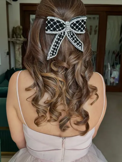 A chic half-up style with a beautiful black and white embellished bow, adding a touch of sophistication to the soft curls.