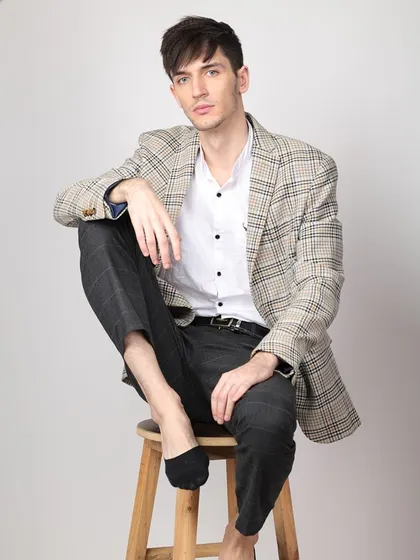 A classic seated portrait for a men's formal wear lookbook. The pose is relaxed yet sophisticated, perfect for showcasing a stylish blazer and shirt combination.