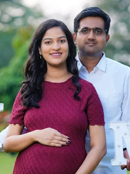 A smiling couple holding "MOM" signs in a park. This is a fun and creative way to celebrate their journey to parenthood during an outdoor photoshoot.