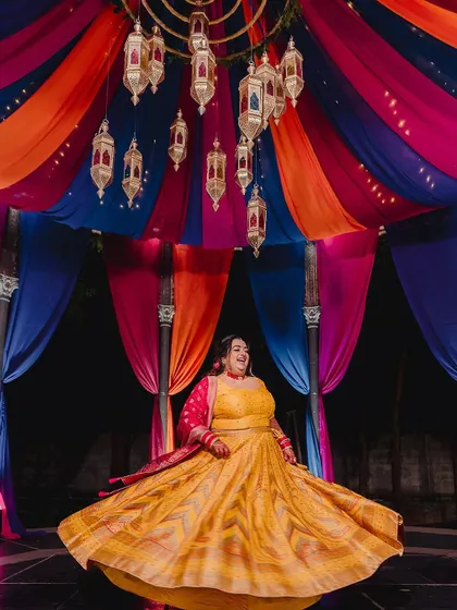 A bride twirling in her vibrant yellow lehenga at a Moroccan-themed Sangeet. The colorful drapes and hanging lanterns create a festive and energetic backdrop.