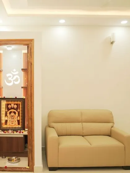 A cozy living room corner with a single-seater sofa next to a custom pooja unit. The design shows how to create functional zones even in smaller spaces.