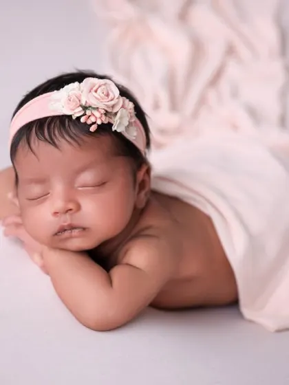 A classic pose on a neutral background with a simple pink wrap and headband. This timeless style focuses entirely on the baby.
