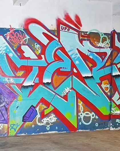 A full view of the red and blue wildstyle piece, flanked by other artists' work, showing a typical collaborative graffiti wall.