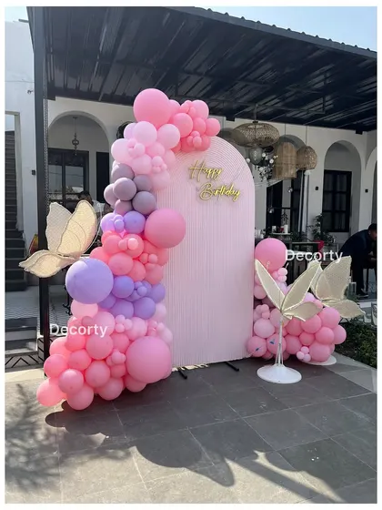 A beautiful butterfly-themed birthday backdrop with pink and purple balloon garlands and large glowing butterfly props.