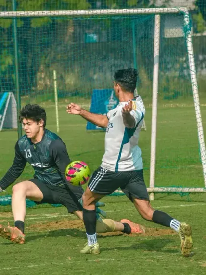 A goalkeeper makes a brave save at the feet of an attacker in a corporate match.