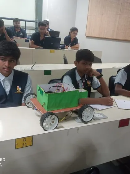 Students prepare their custom-built robots at their desks during a robotics fest, getting ready for their turn on the competition floor.