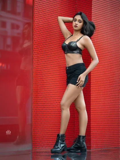 A full-body standing pose that showcases the model's confident attitude. The bright red background makes this a powerful and eye-catching urban portrait.