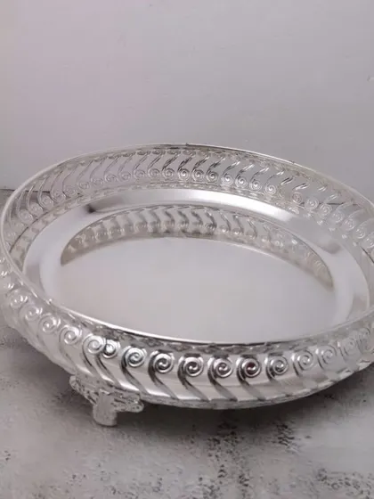 A German silver tray with a swirled pattern on the rim and small legs. It's a beautiful base for arranging pooja items.