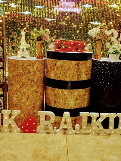 A personalized anniversary celebration with marquee letters spelling out the couple's names in front of a glamorous gold backdrop and themed pedestals.