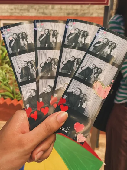A hand holding a fan of photo strips, some with cute heart stickers added for a personal touch.