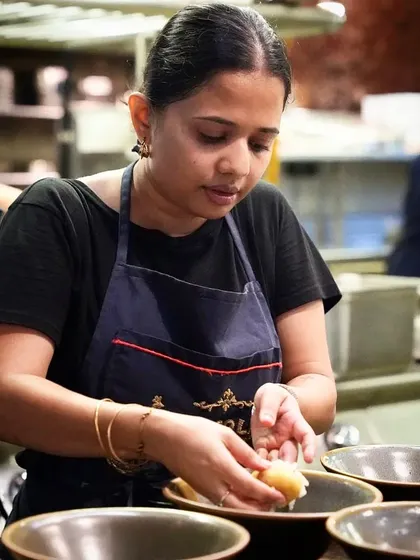 A female chef carefully assembling a dish, showing the focus and delicate touch required in a professional kitchen. This image celebrates the diverse talent behind great food.