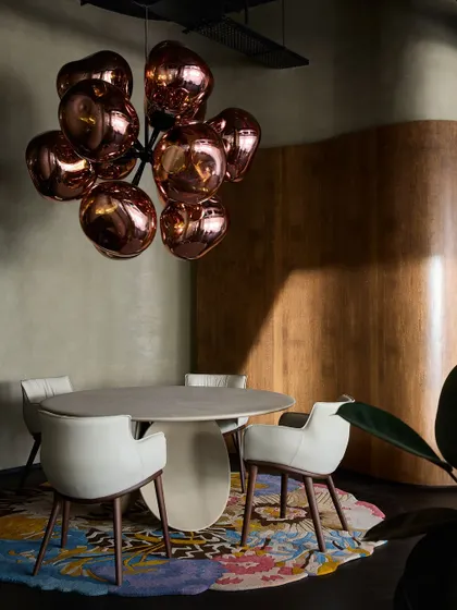 A dramatic dining vignette featuring a sculptural copper-toned chandelier over a simple round table. The curved wood wall in the background adds warmth and texture.