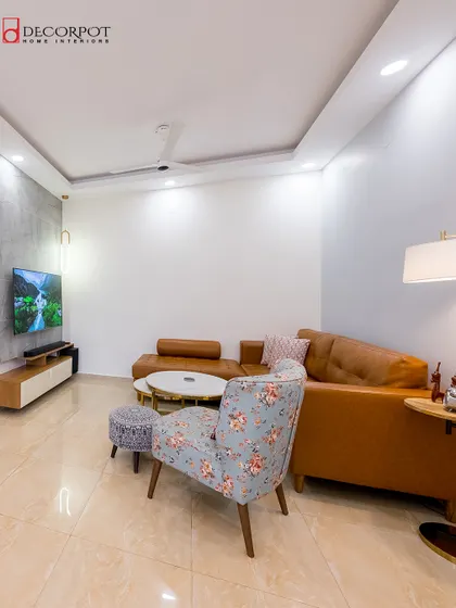 A cozy living room setup with a tan leather sofa and a floral accent chair. The minimalist TV unit and simple decor create a clean and uncluttered look, perfect for a relaxed family space.