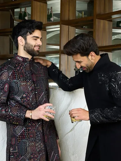A moment of camaraderie, featuring two distinct yet complementary black kurtas. One is adorned with the hand-embroidered cheetah, the other with a complex, multi-hued pattern.